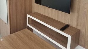 A modern room with a built-in TV, a wooden cabinet, and a white-framed shelf.