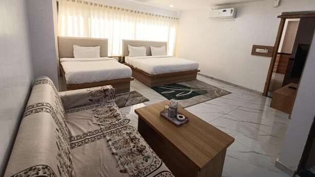 A hotel room with two beds, a sofa, a coffee table, and a ceiling fan.