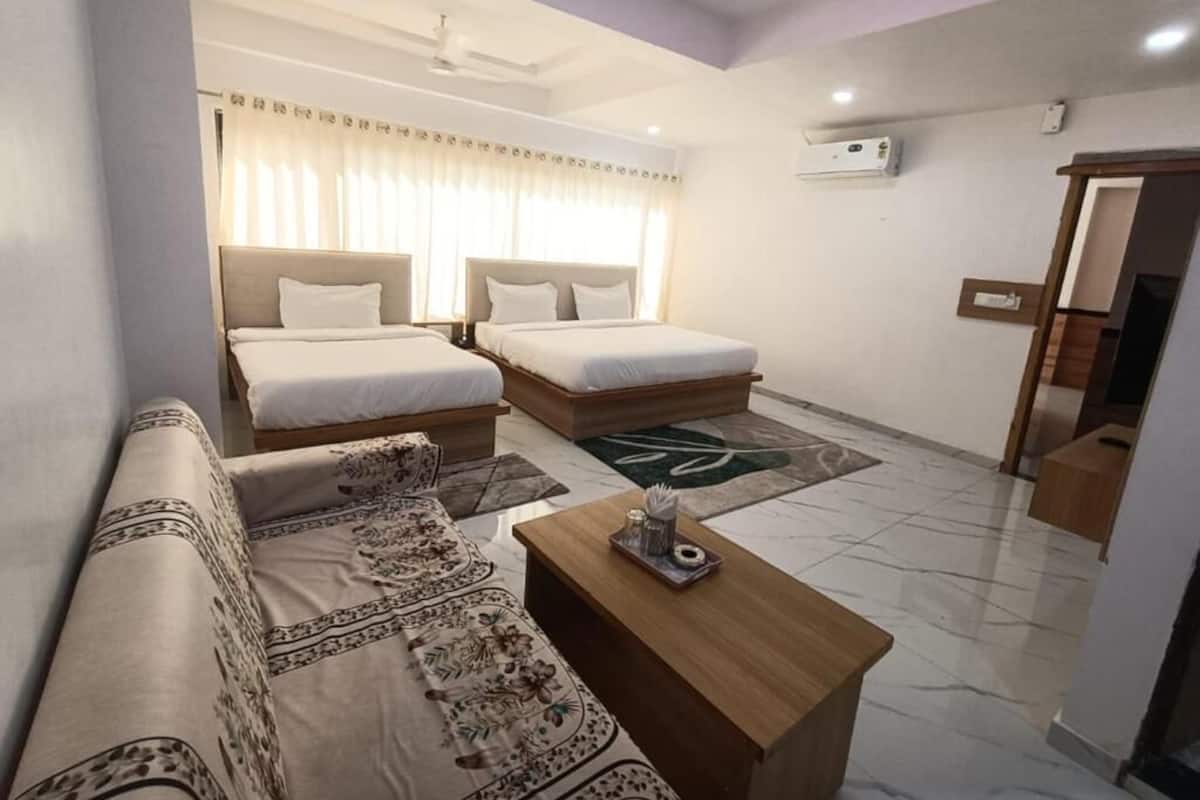 A hotel room with two beds, a sofa, a coffee table, and a ceiling fan.