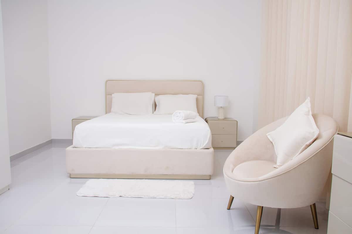 A bedroom with a bed, a chair, a nightstand, and a lamp.