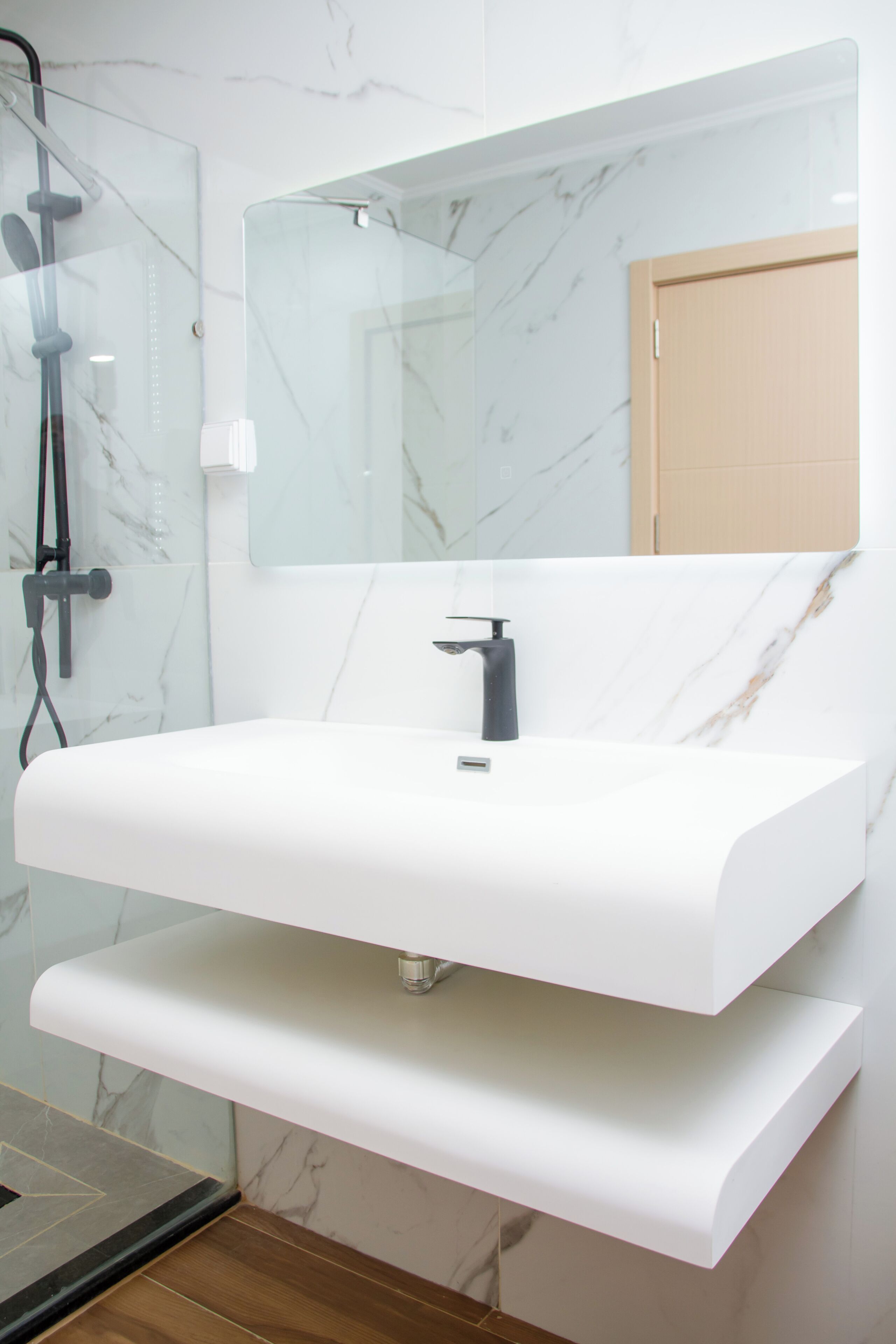 Ein modernes Badezimmer mit einem weißen Marmorwaschbecken, einem Spiegel und einer Dusche.