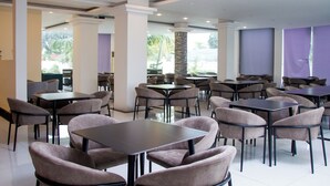 A spacious indoor dining area with multiple tables and chairs, large windows, and a view of the outdoors. - Hotel Kilimanjaro (Luanda)