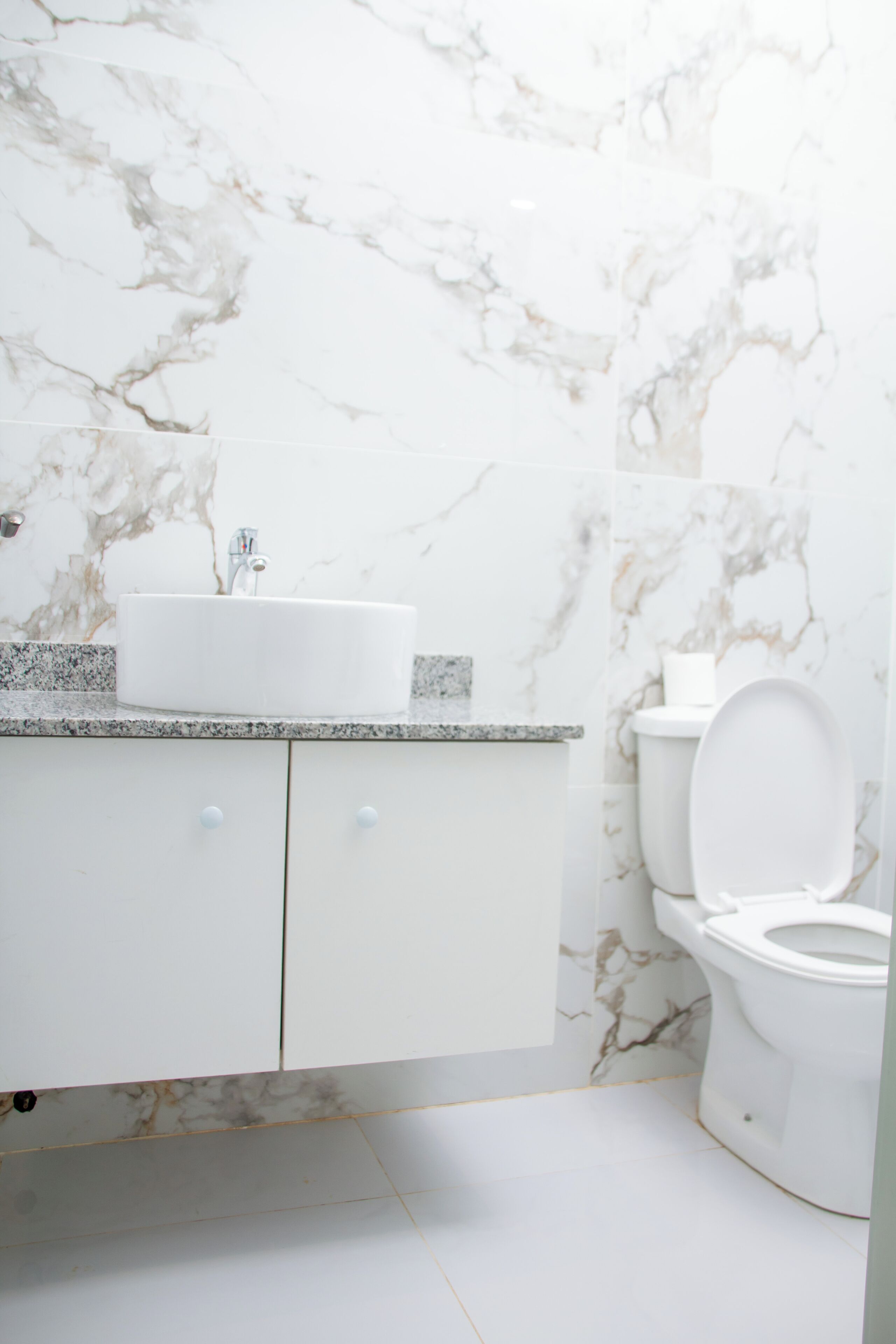 A bathroom with a marble wall, a white sink, and a toilet.