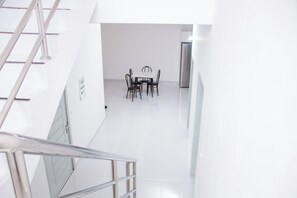 A modern interior with a staircase, a dining area with a table and chairs, and a refrigerator.