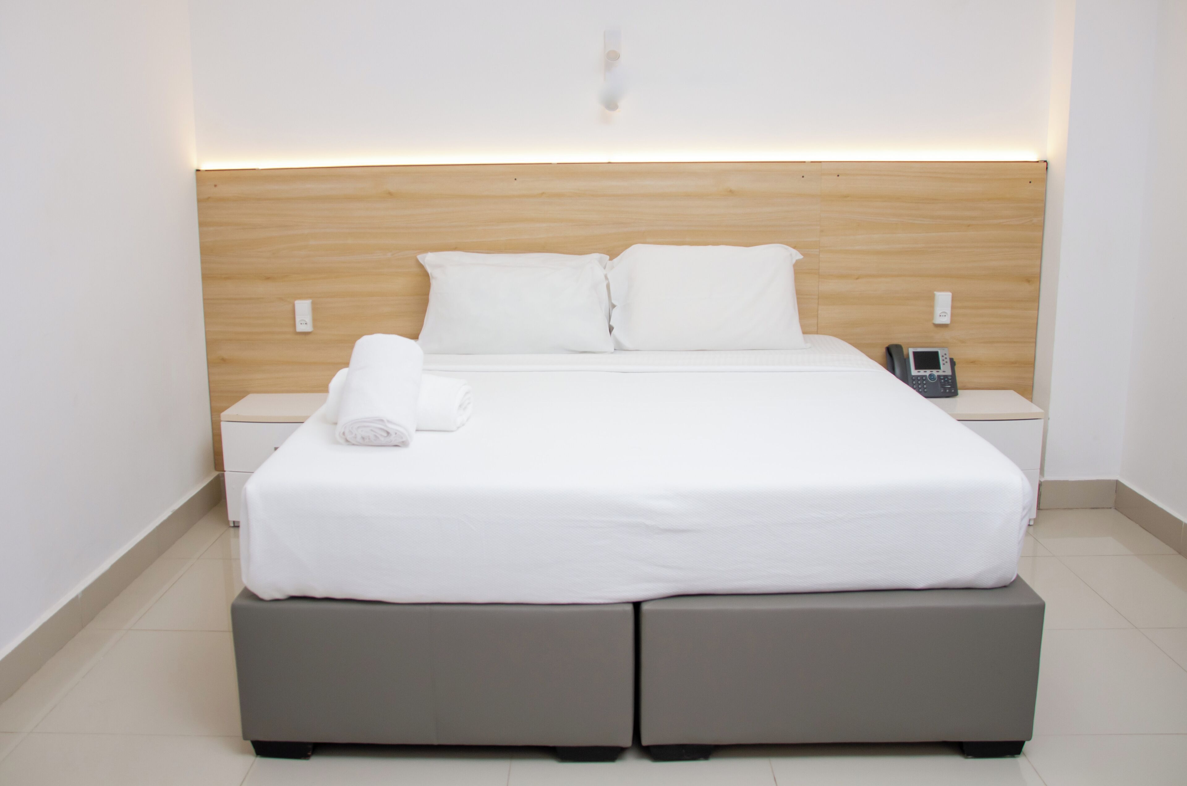 A neatly made bed with white linens, a bedside phone, and a wooden headboard.
