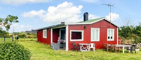 Ein rotes Gebäude mit einer überdachten Veranda, einem Schornstein und einem Tisch mit Stühlen davor.