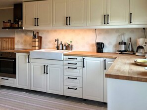 A kitchen with white cabinets, a wooden countertop, a built-in oven, and various appliances. - 4 Person Holiday Home in Borgholm (Borgholm)