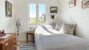 Ein Schlafzimmer mit einem Bett, einem Fenster, einer Heizung, einer Holzkommode und einem Ventilator.