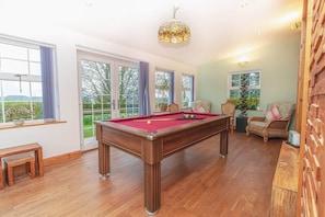 A pool table in a room with large windows, a bench, and wicker furniture.