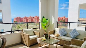 A balcony with wicker furniture, a glass table, and a view of red buildings. - Apartamento Sea Blue D D by At Home Costa del Sol (Torrox)