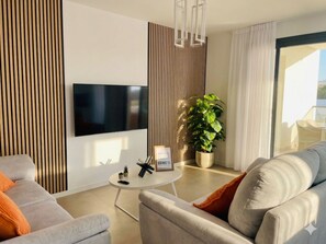 Un saló modern amb televisió plana, una taula de centre rodona, un sofà, una planta en test i una porta corredissa de vidre.