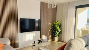 A modern living room with a flat-screen TV, a round coffee table, a sofa, and a potted plant. - Apartamento Sea Blue D D by At Home Costa del Sol (Torrox)