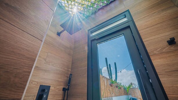 Ein modernes Zimmer mit Holzwänden, einem Oberlicht, einem großen Fenster und Blick auf Kakteen vor dem Fenster.