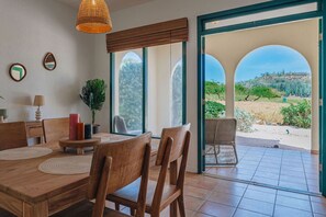 Ein Essbereich mit Holztisch und Stühlen, einer Hängelampe und Blick durch eine Glastür auf eine Terrass.