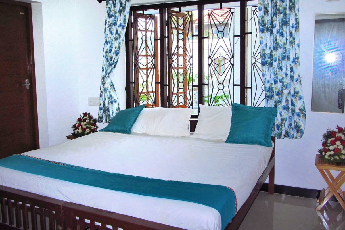 Una cama con ropa de cama blanca y aguamarina, un cabecero de madera y una ventana con barrotes y cortinas.
