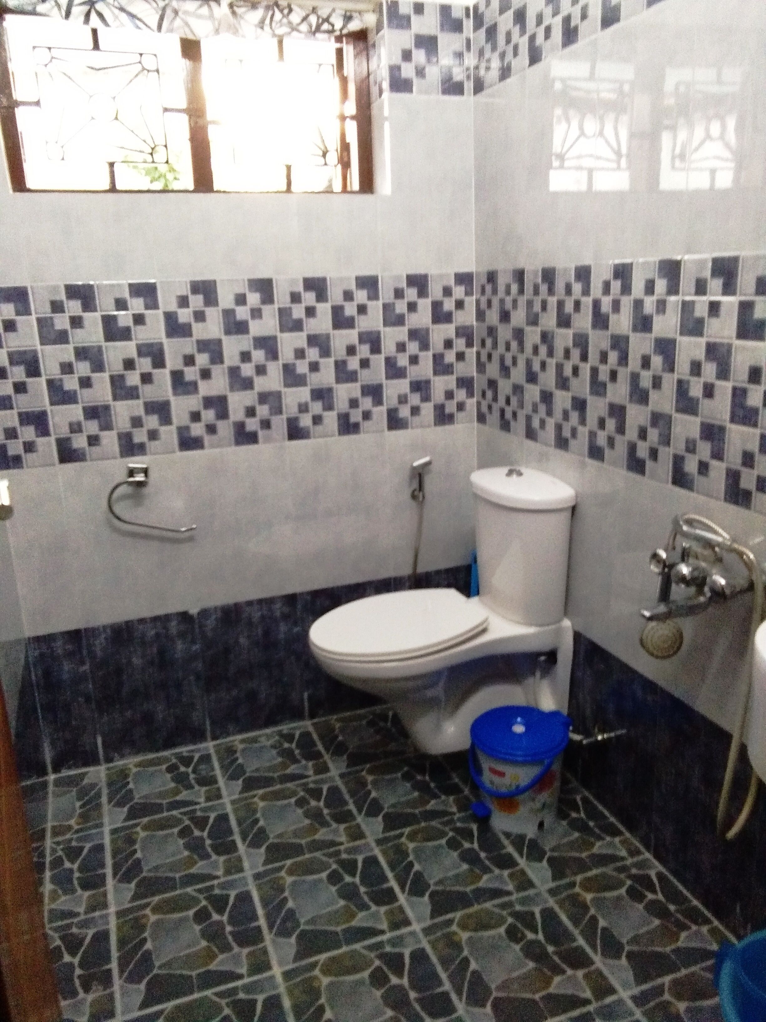 Ein Badezimmer mit Toilette, Waschbecken und Dusche. Die Wände sind mit einem blau-weißen Muster gefliest.