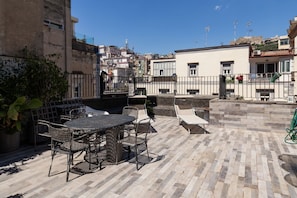 A rooftop patio with a table and chairs, a small seating area, and a view of the cityscape. - Chiaia 74 Rooftop By Dimorra (Naples)
