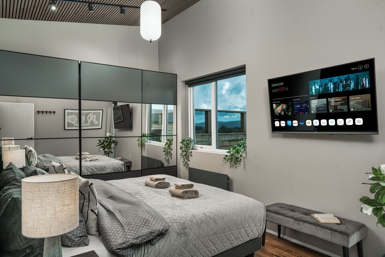 Ein modernes Schlafzimmer mit einem großen Spiegel, einem Flachbildfernseher und einem Fenster mit Blick.