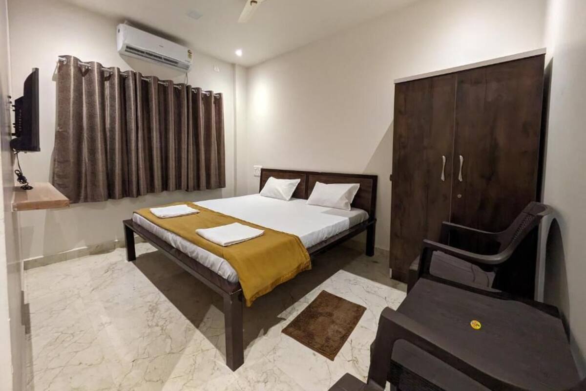 A bedroom with a bed, a desk, a wardrobe, and an air conditioning unit.