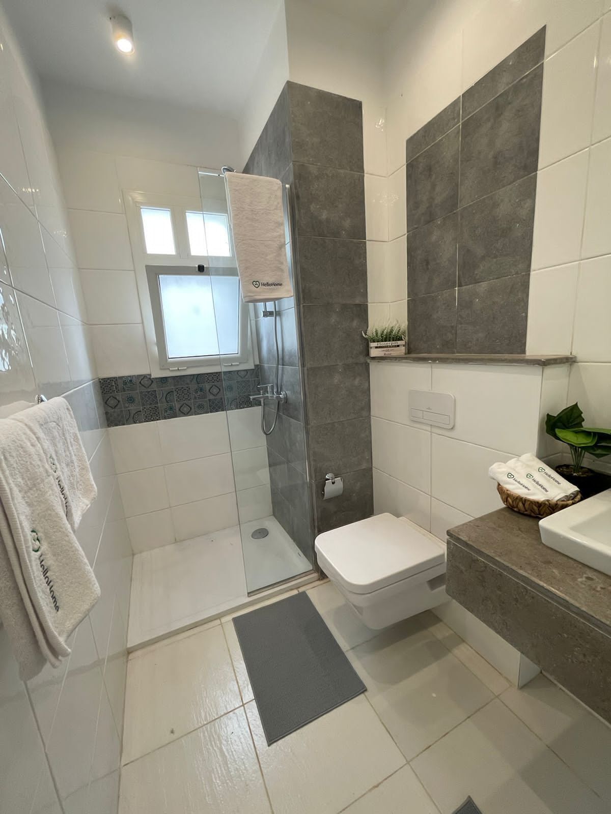 Une salle de bain moderne avec une douche à parois de verre, des toilettes, un lavabo et une fenêtre.