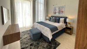 Un dormitorio moderno con una cama grande, mesitas de noche, un escritorio y un cuadro en la pared.
