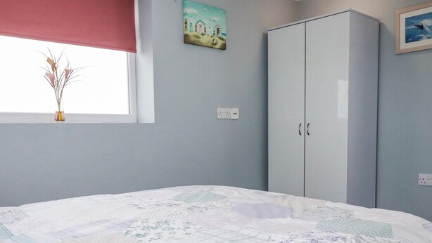 A bedroom with a bed, a wardrobe, a window with a view, and a painting on the wall. - Likely Sunset (St Austell)