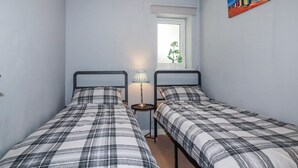 Un dormitorio con dos camas, una mesita de noche con lámpara, una ventana con vistas a zonas verdes y un cuadro en la pared.