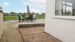 A patio area with a table and chairs, a view of a horse, and a building with a large window. - Likely Sunset (St Austell)