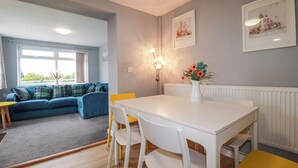 A dining area with a white table and chairs, a blue sofa with green cushions, and a vase with flowers. - Likely Sunset (St Austell)