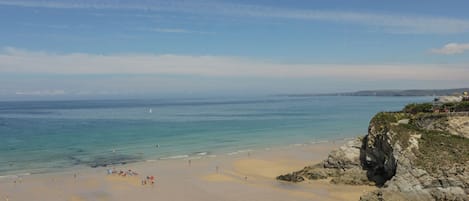 Una playa con cielos despejados, aguas tranquilas y acantilados rocosos.