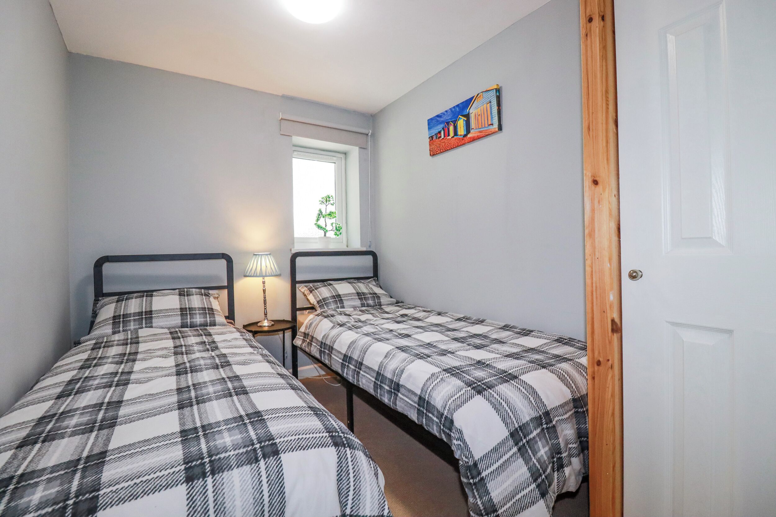 Un dormitorio con dos camas, una ventana, una lámpara y una puerta.