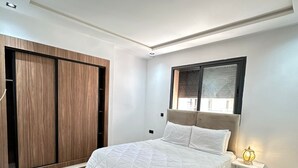 Ein modernes Schlafzimmer mit einem großen Bett, einem Kleiderschrank, einem Nachttisch und einem Fenster mit Jalousien.