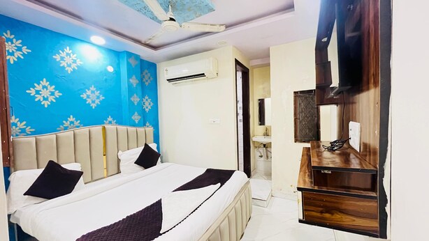 A hotel room with a bed, a vanity with a mirror, an air conditioning unit, and a ceiling fan. - Roomshala NP International (New Delhi)