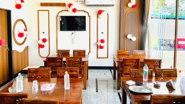 Un comedor de hotel con mesas y sillas de madera, un candelabro, un televisor de pantalla plana y globos decorativos.