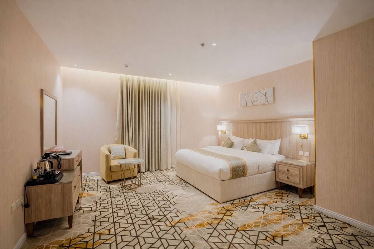 Una habitación de hotel moderna con una cama grande, mesitas de noche, una silla, un escritorio con teléfono y un piso con diseño.