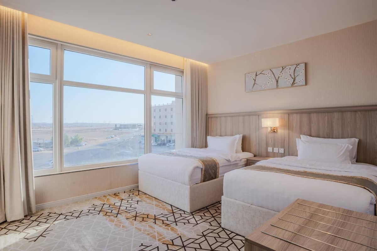Habitación de hotel con dos camas, un ventanal con vistas, suelo estampado y una pequeña mesa.