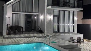 Una casa moderna de dos pisos con piscina, mobiliario exterior y un balcón.