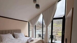 Un dormitorio con cama, un ventanal grande, vistas al exterior y una lámpara en el techo.