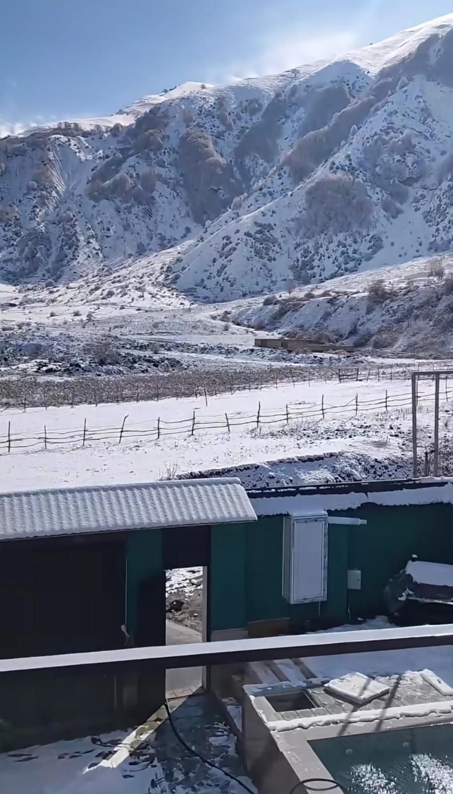 Eine Berglandschaft mit schneebedeckten Gipfeln und einem Gebäude mit Wellblechdach.