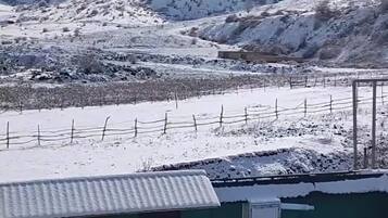 Eine Berglandschaft mit schneebedeckten Gipfeln und einem Gebäude mit Wellblechdach.