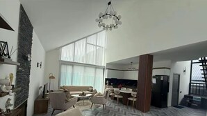 Un amplio salón con suelo de espiga, una chimenea, un sofá, una mesa de comedor con sillas y una cocina al fondo.