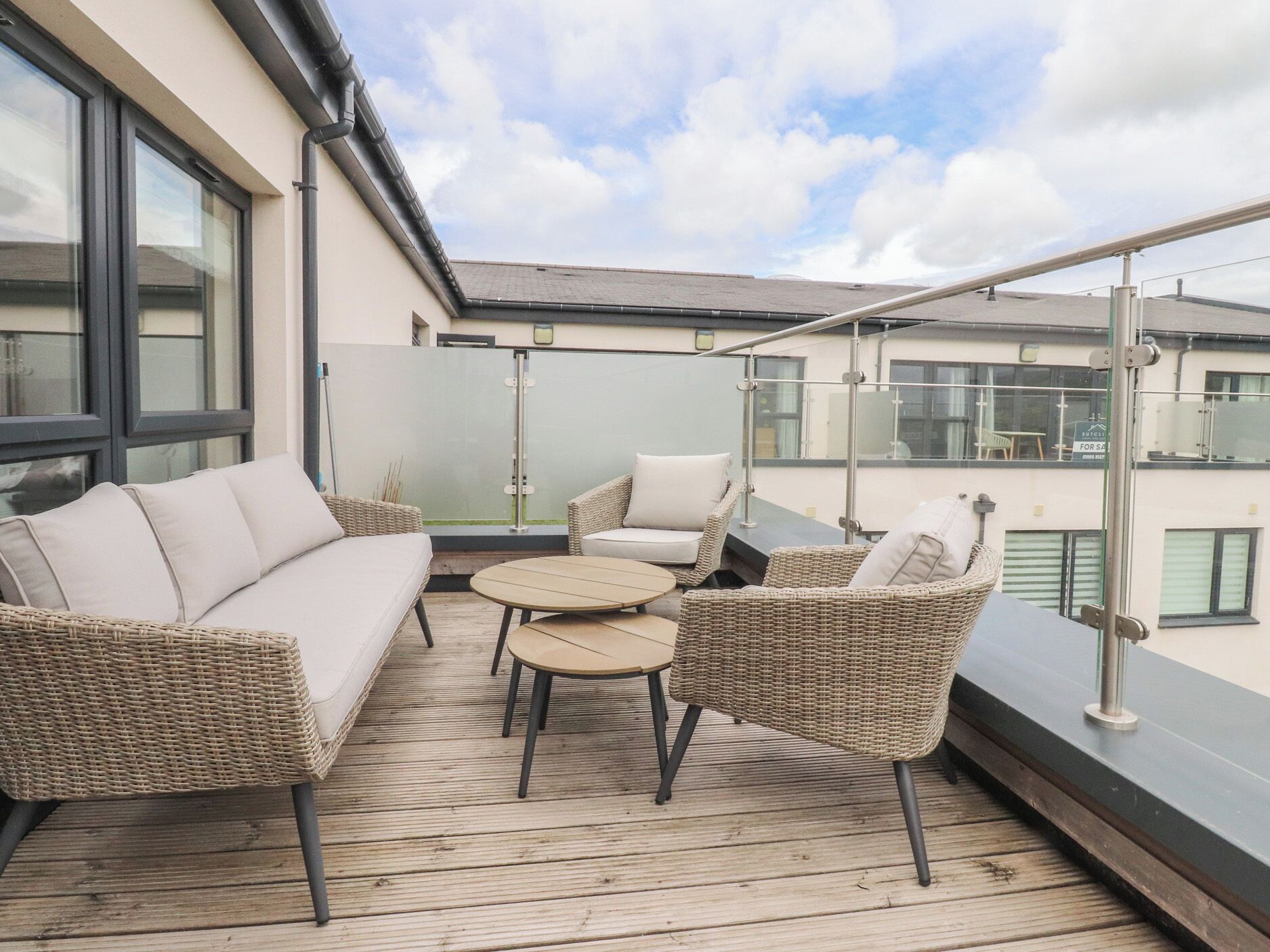Een balkon met rieten meubilair, een glazen deur en uitzicht op gebouwen.
