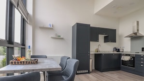 A modern kitchen with dark cabinets, a built-in oven, and a dining area with a table and chairs. - Apartment 20, River View (Preston)