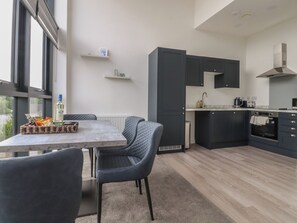 A modern kitchen with dark cabinets, a built-in oven, and a dining area with a table and chairs. - Apartment 20, River View (Preston)