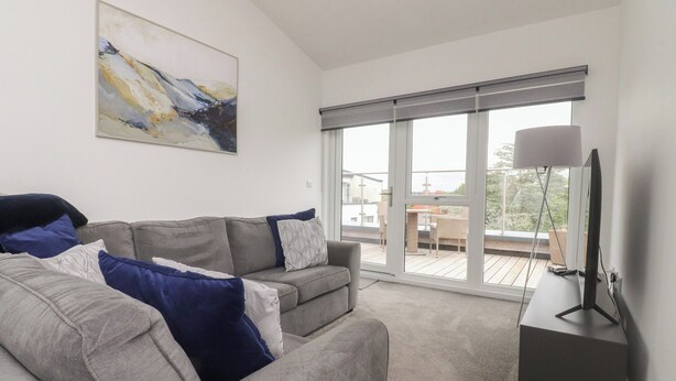 A modern living room with a grey sofa, a flat-screen TV, and a large window with a view of the outdoors. - Apartment 20, River View (Preston)