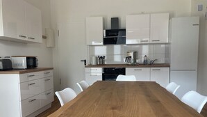 A modern kitchen with white cabinetry, a wooden dining table, and white chairs. - Urban & close to nature at Alter Bahnhof near Hamburg Bright apartment with 3 bedrooms (Trittau)