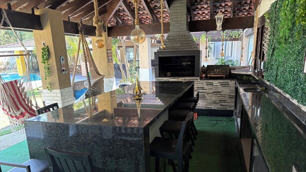A bar area with a stone counter, bar stools, a hanging light fixture, and a view of a pool. - Luxury Mansion in Barra / Sleeps 50 + Events, Gated Community + 24-hour Security (Rio de Janeiro)