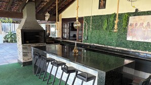 An outdoor kitchen with a stone countertop, bar stools, and hanging lights. - Luxury Mansion in Barra / Sleeps 50 + Events, Gated Community + 24-hour Security (Rio de Janeiro)