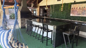 A bar area with a green artificial turf floor, black bar stools, and a hanging hammock. - Luxury Mansion in Barra / Sleeps 50 + Events, Gated Community + 24-hour Security (Rio de Janeiro)