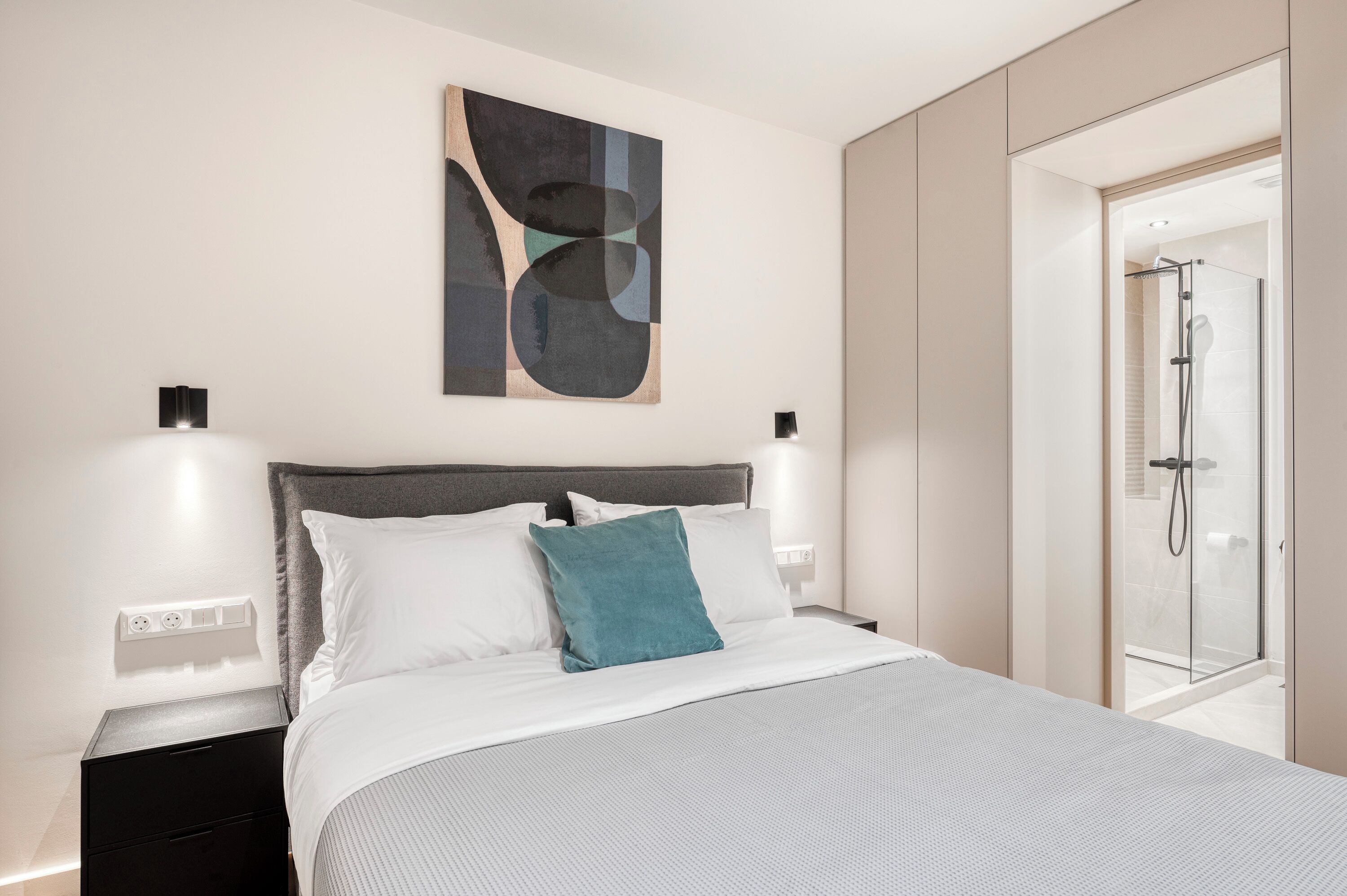 A modern hotel room with a large bed, a shower, and a wall-mounted abstract art piece.